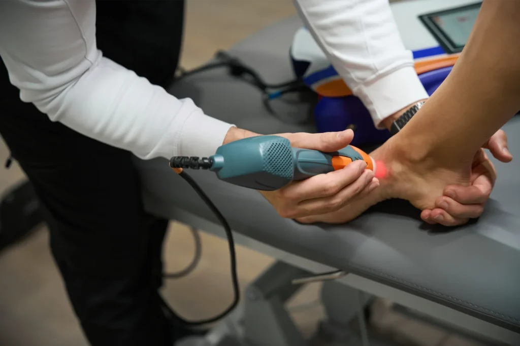 Physical therapist using a laser therapy device on a patient’s hand to reduce pain and inflammation.