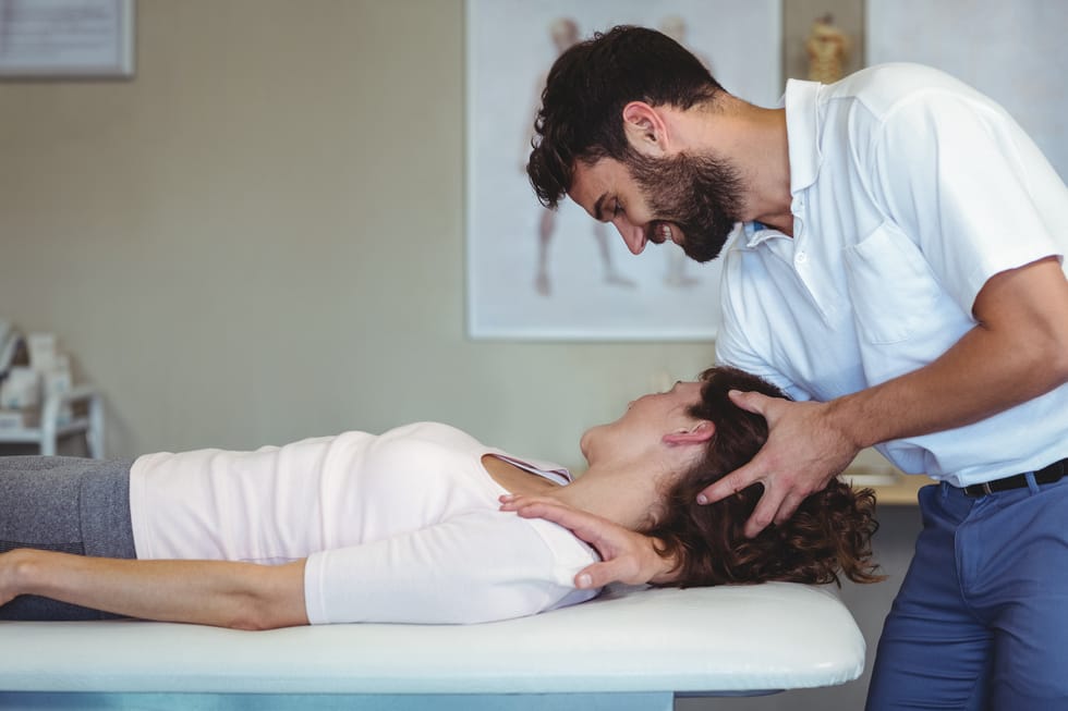 A chiropractor providing neck treatment to a woman on a therapy table in a professional clinic.